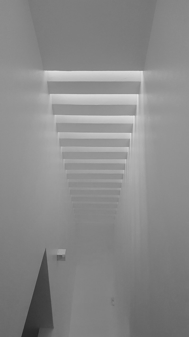 Looking up at a series of horizontal louvers filtering daylight into a white plastered ceiling void