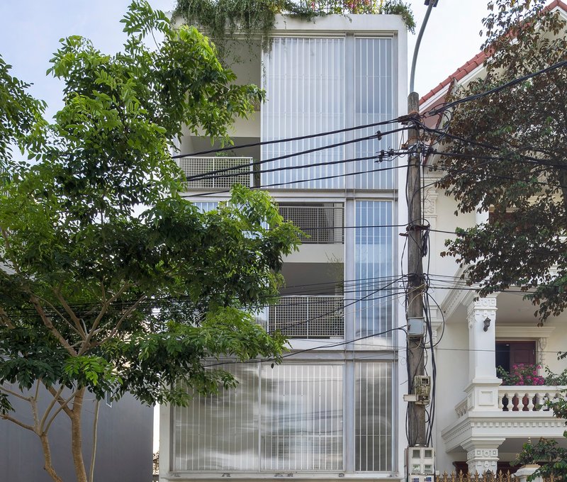 Street view of the vertical corrugated facade with perforated metal balconies framed by neighboring trees