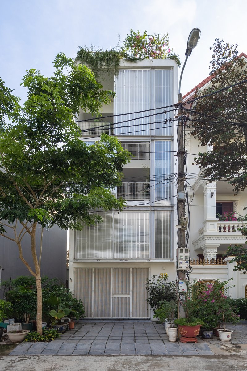 Front elevation showing the translucent corrugated cladding and balconies with potted plants on paving below