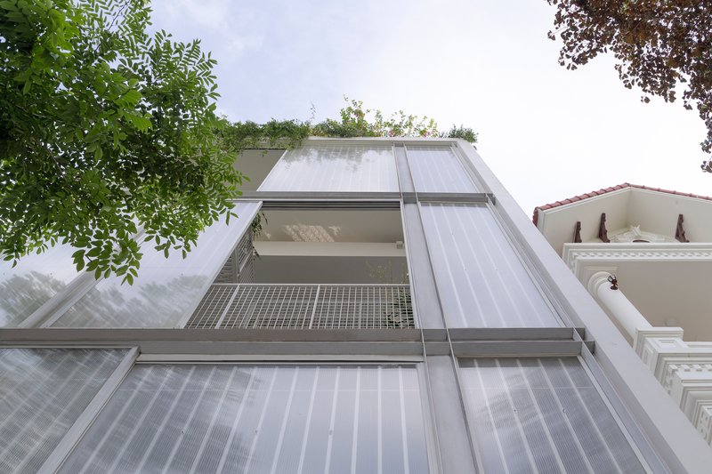 Upward view of the translucent polycarbonate and mesh facade with metal frame between tree branches