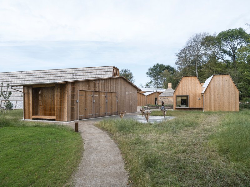 Collection of timber-clad pavilions with varied gabled roofs arranged around a gravel path and meadow planting
