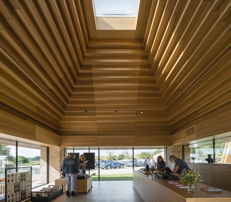Reception desk beneath a stepped timber ceiling with central skylight and visitors inside