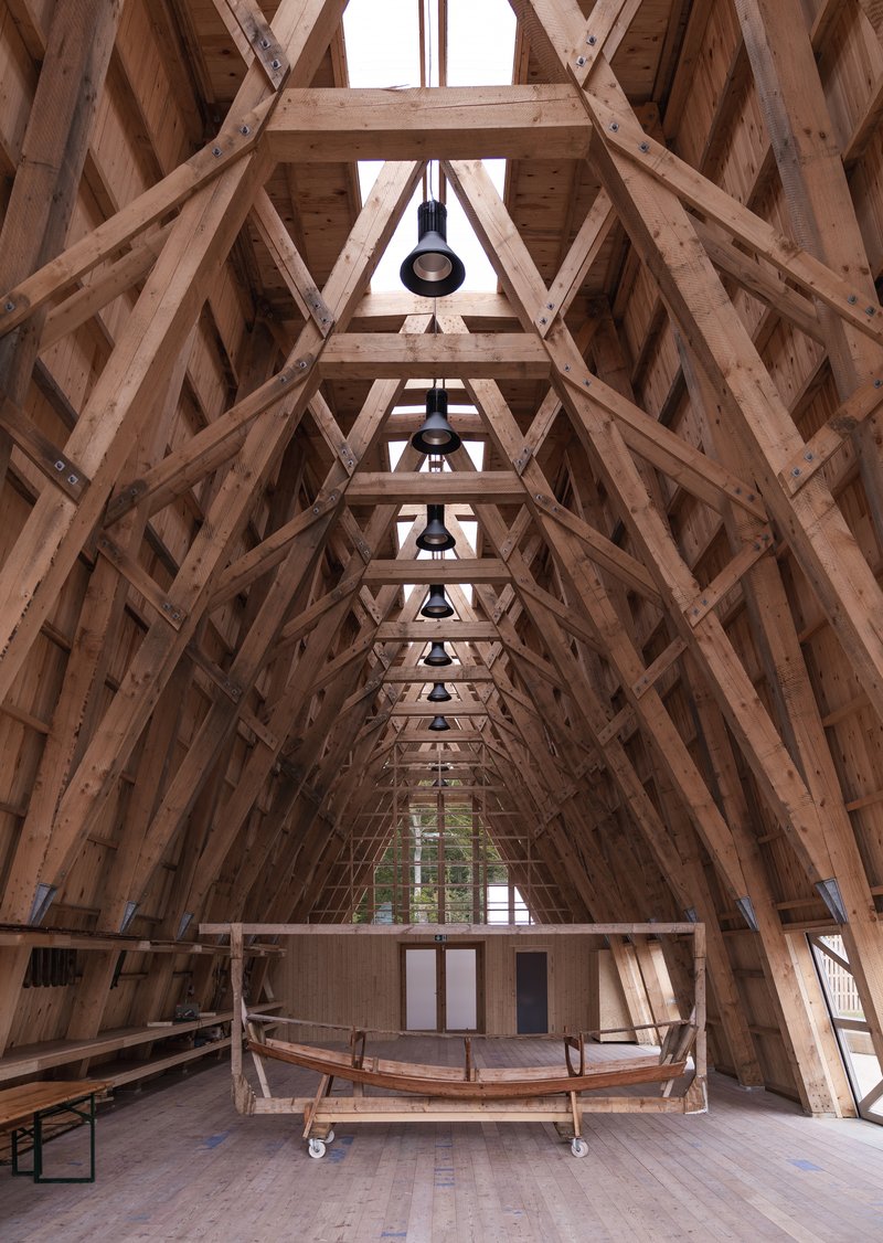 Upward view of exposed timber truss structure with repeated diagonal bracing and hanging pendant lights