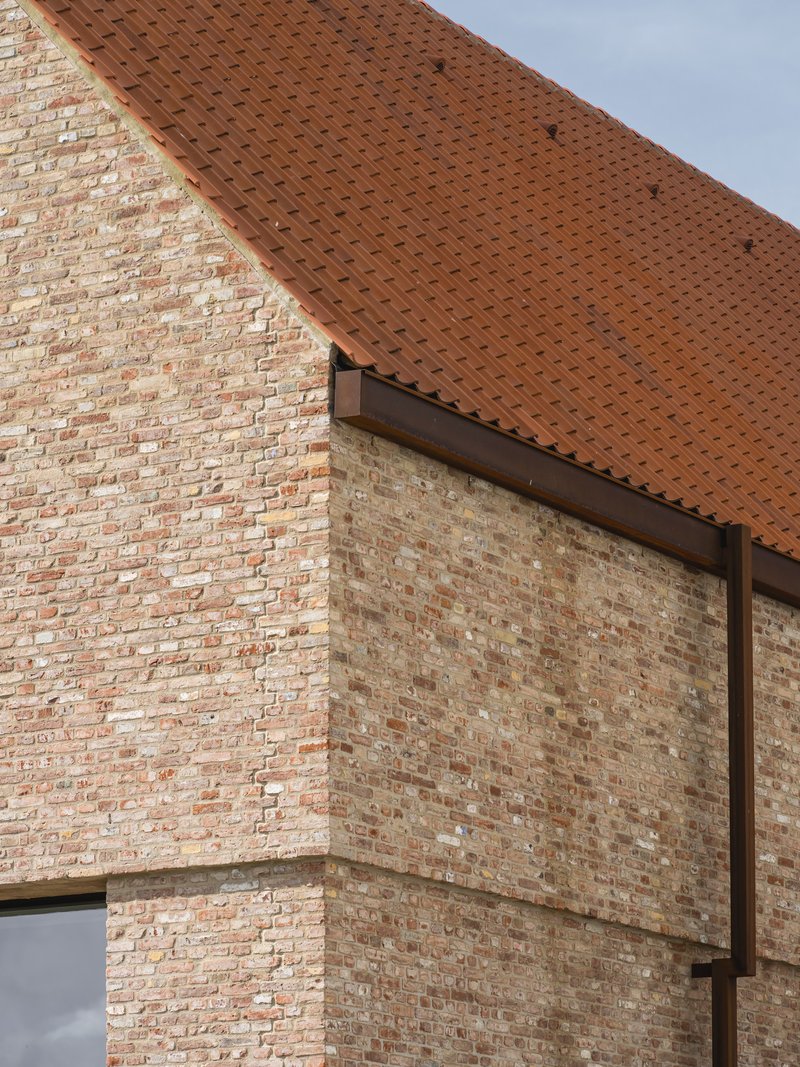 Corner detail of brick masonry gable wall meeting clay tile roof under overcast sky