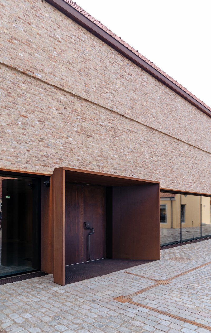 Recessed steel-framed entrance with timber door set into brick facade along paved walkway