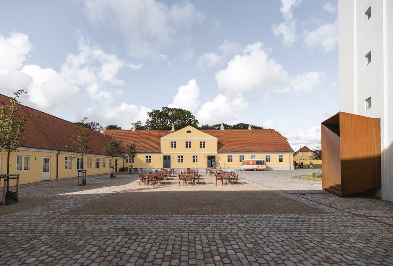 Cobblestone courtyard surrounded by yellow buildings with outdoor seating under a partly cloudy sky