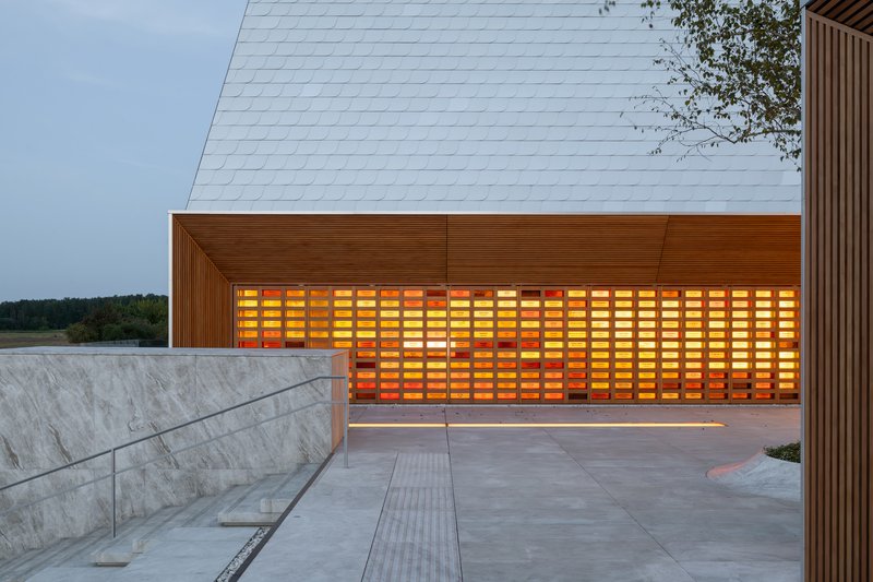 Covered entrance with illuminated amber glass block wall and timber ceiling at dusk