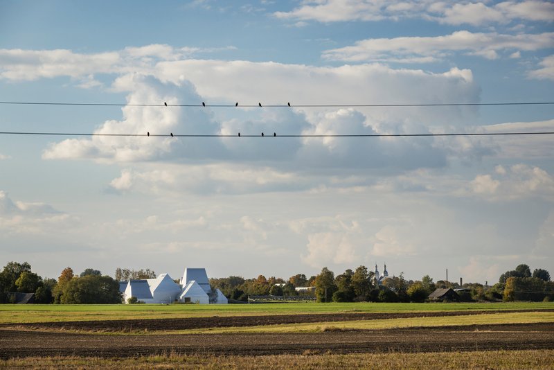 Distant view of the white clustered volumes across ploughed fields with birds on a wire