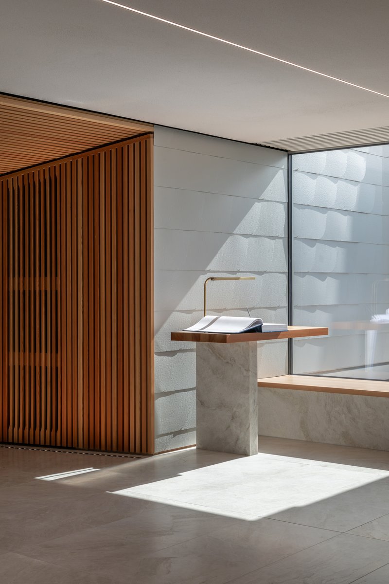 Interior lectern of concrete and timber beside vertical wood slat wall with sunlight filtering through