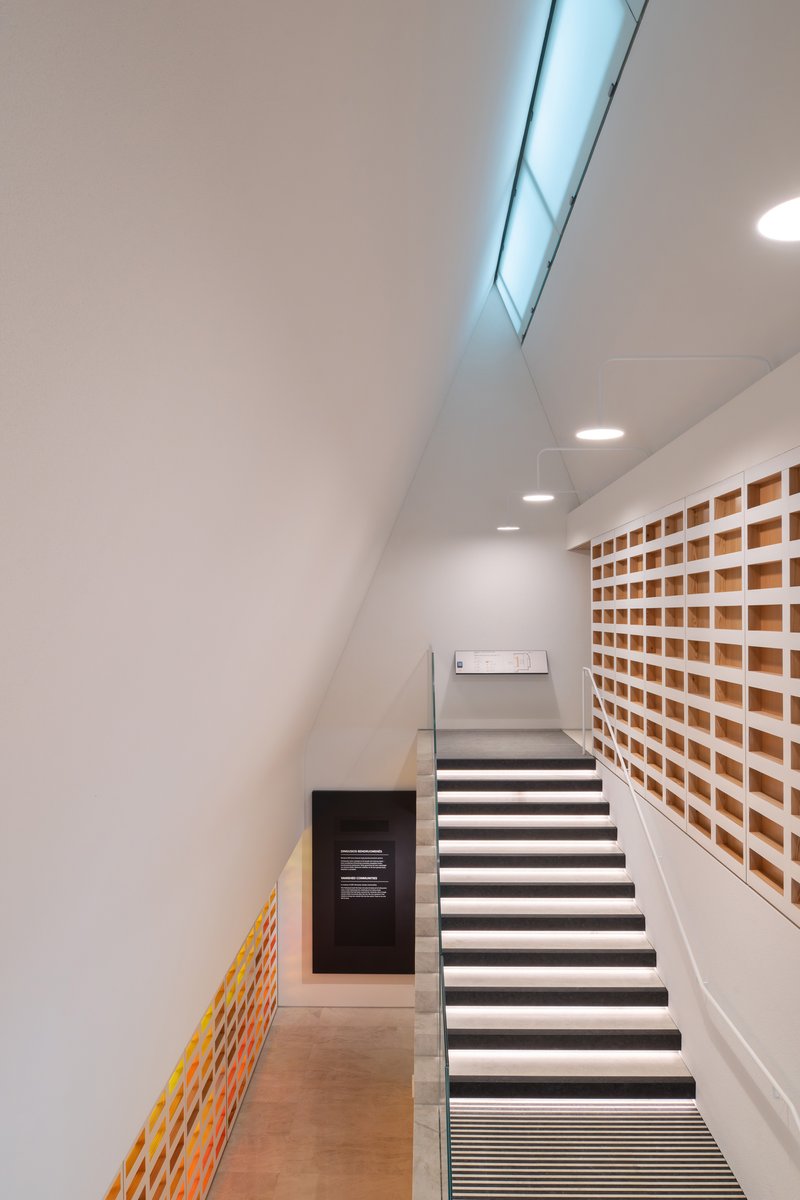 Interior staircase with illuminated treads and a slatted wood niche wall under a skylight