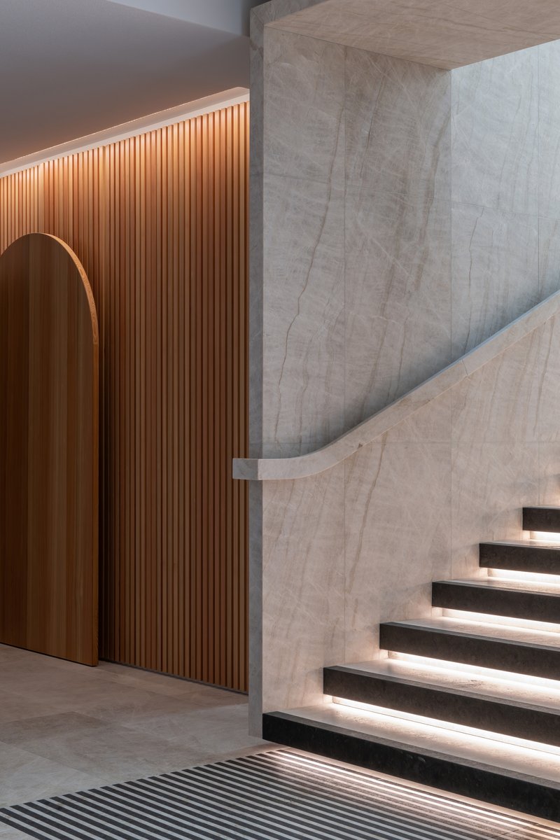 Junction of curved timber wall with arched opening and board-formed concrete stair with lit treads