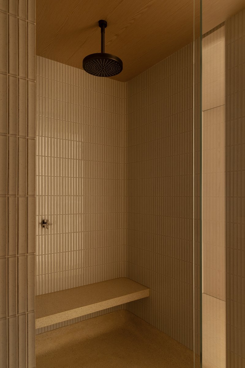 Shower enclosure with vertical ribbed tile walls, ceiling-mounted rainfall head and wooden bench