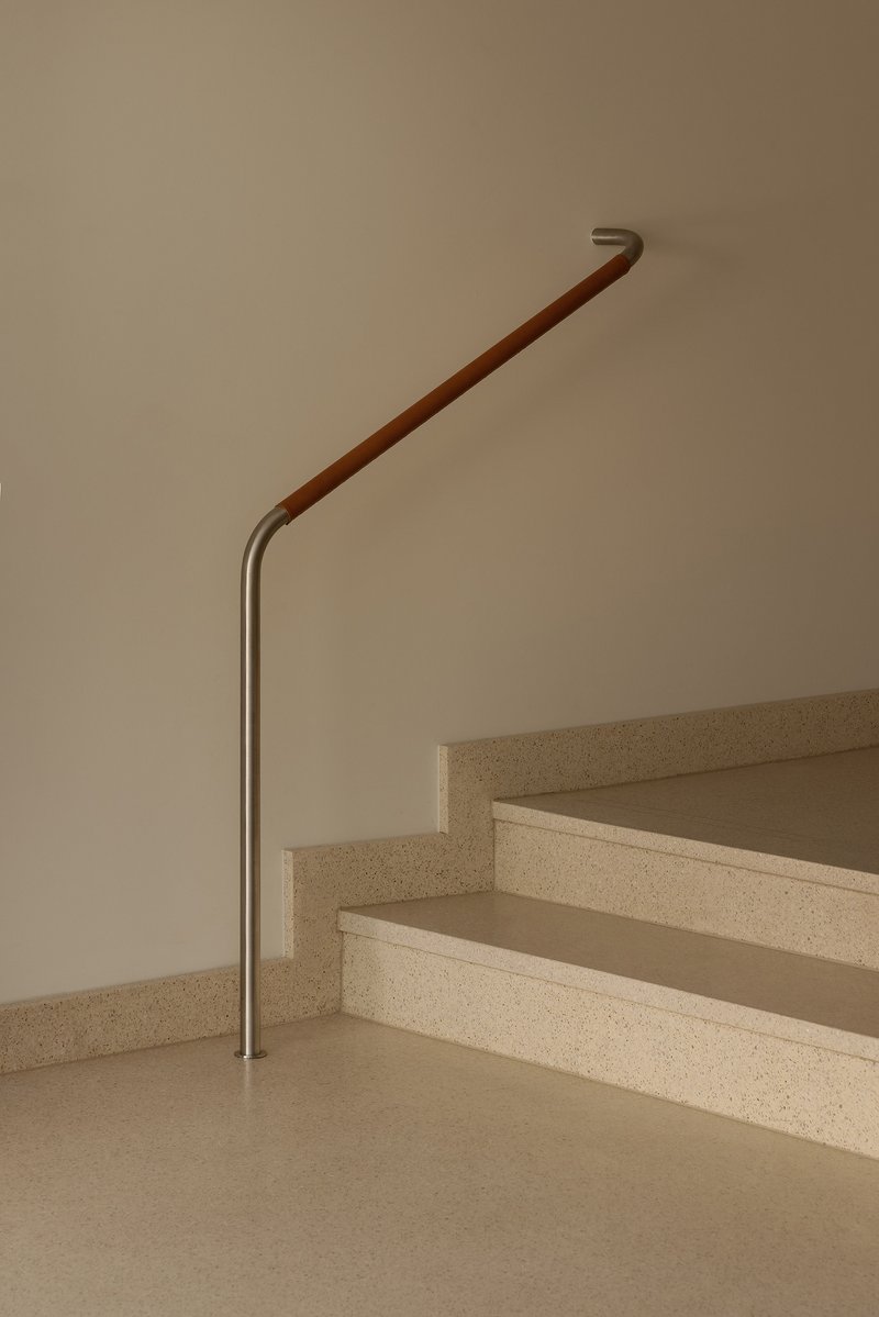 Staircase with terrazzo treads and leather-wrapped handrail terminating at brushed metal base