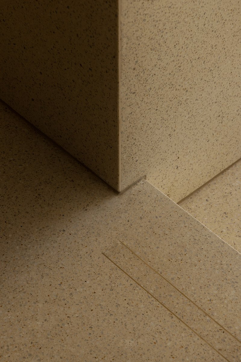 Close-up of terrazzo flooring meeting a wall corner with integrated drainage channel under warm light