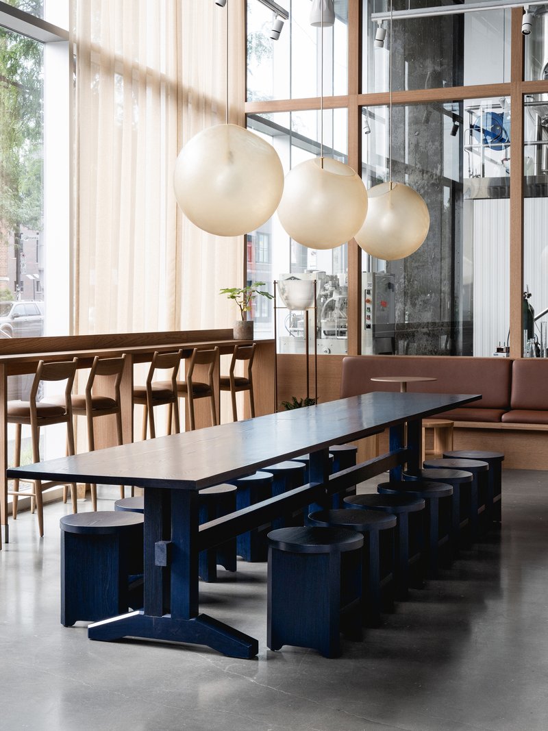 Communal table in navy-painted timber with cylindrical stools beneath clustered globe pendants and sheer curtains