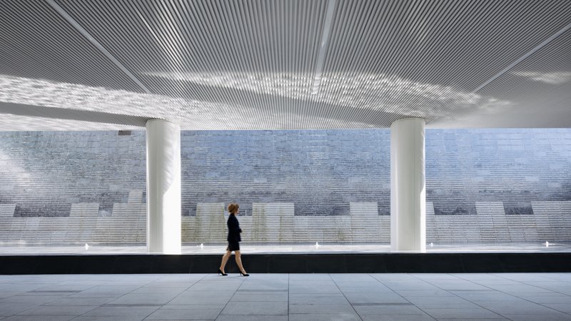 Covered walkway with ribbed ceiling and white columns as a person passes the pixelated tile wall