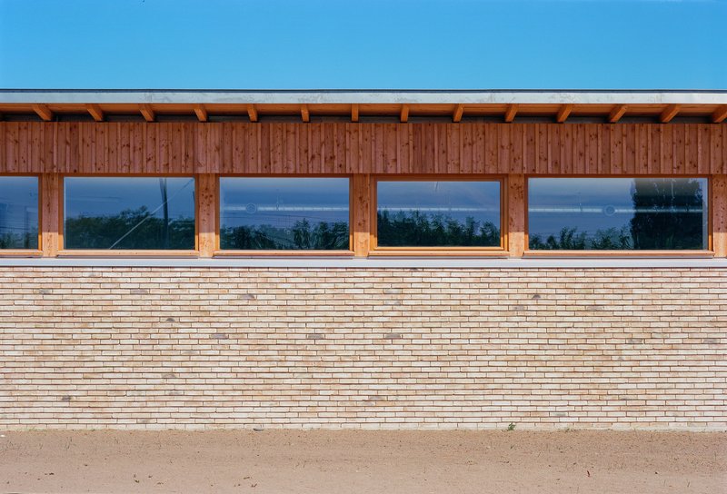 Facade detail showing horizontal timber planks beneath vertical wood cladding and a row of picture windows at dusk