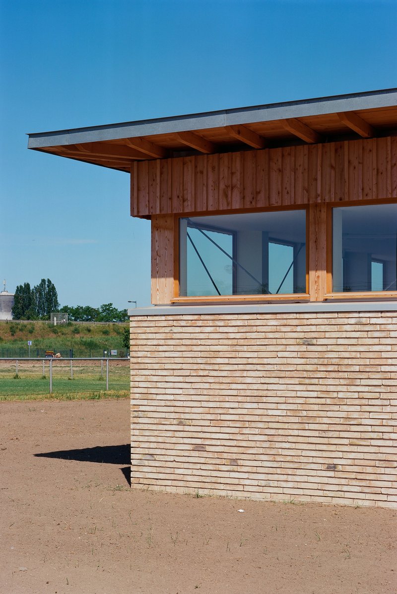 Corner detail of horizontal timber cladding with exposed rafters and a ribbon window above the sports field