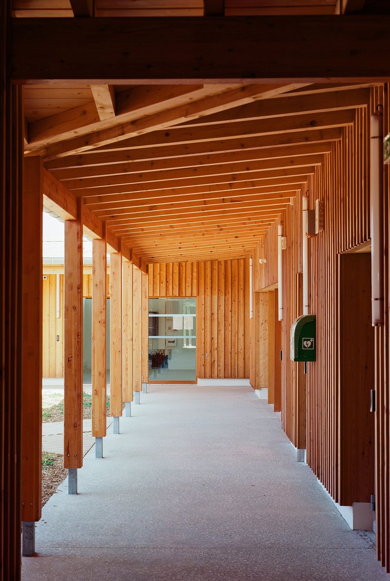 Covered timber colonnade with exposed beam ceiling and vertical slat wall catching afternoon light