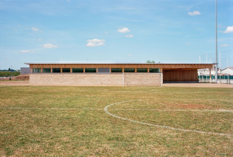 Long facade with horizontal timber clerestory above a pale brick base facing the sports field