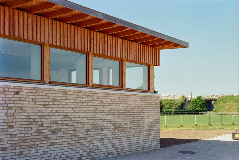 Corner detail showing vertical timber cladding above tan brick with glazed openings under overhanging eaves