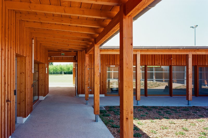 Covered walkway with exposed timber columns and beams framing views through to the glazed interior