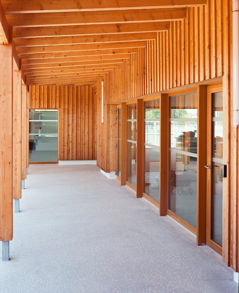 Timber-clad corridor with glazed doors, vertical slat screen, and exposed beam ceiling in daylight