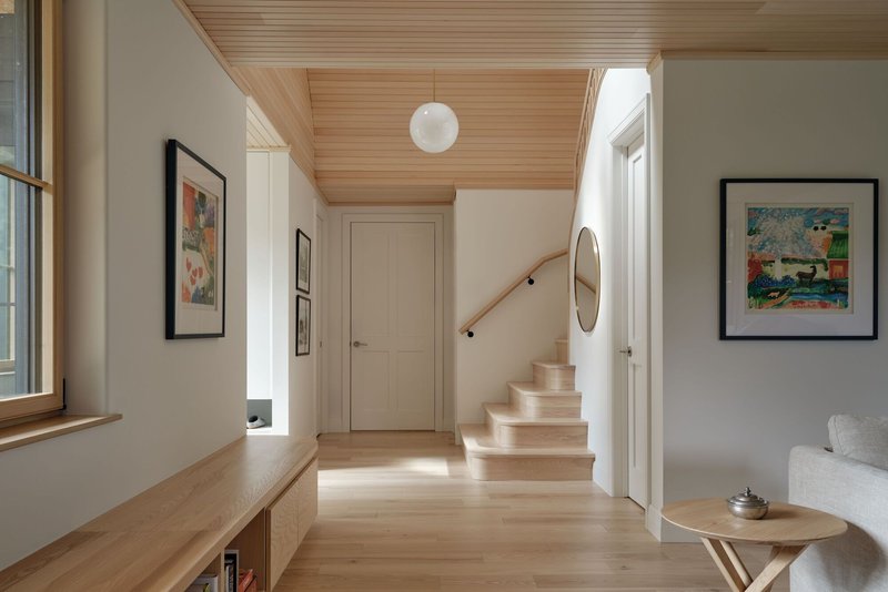 Interior hallway with wood-clad ceiling, pale timber stair and globe pendant casting sunlight across the floor
