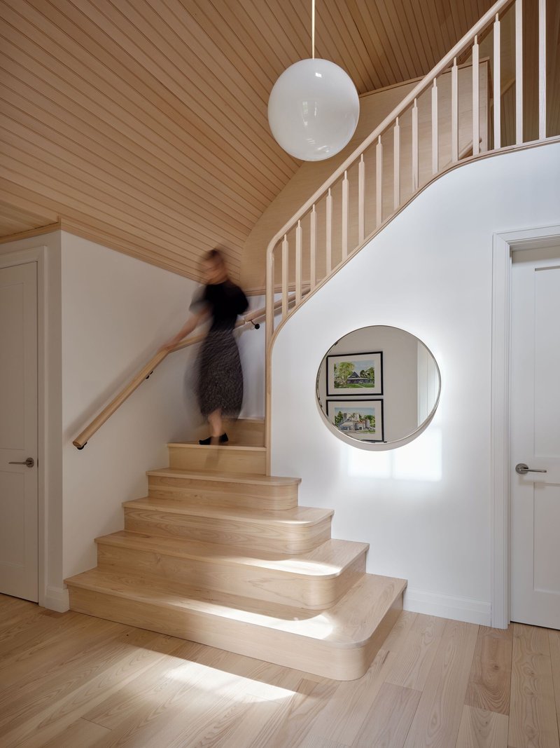 Staircase with circular porthole window in the wall and a figure ascending under the vaulted timber ceiling