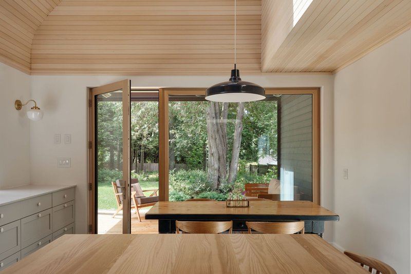 Dining area with timber table and pendant light looking out to green garden through glazed doors