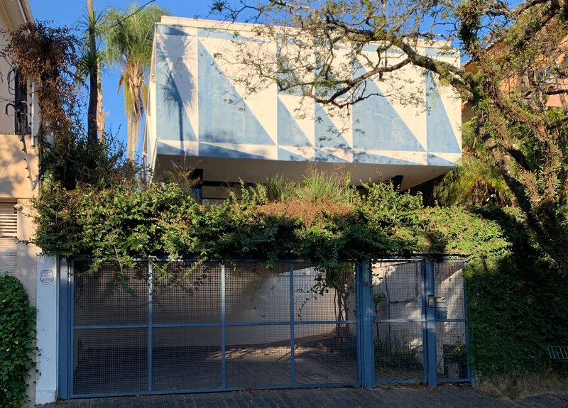 View from street showing cantilevered volume with geometric facade behind mesh gate and bare tree