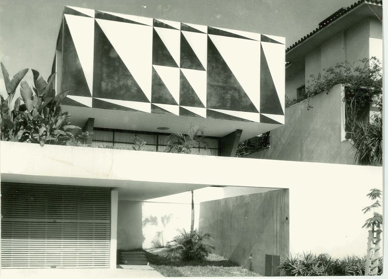 Upper volume with geometric triangular facade panels above a recessed entry courtyard with planted beds