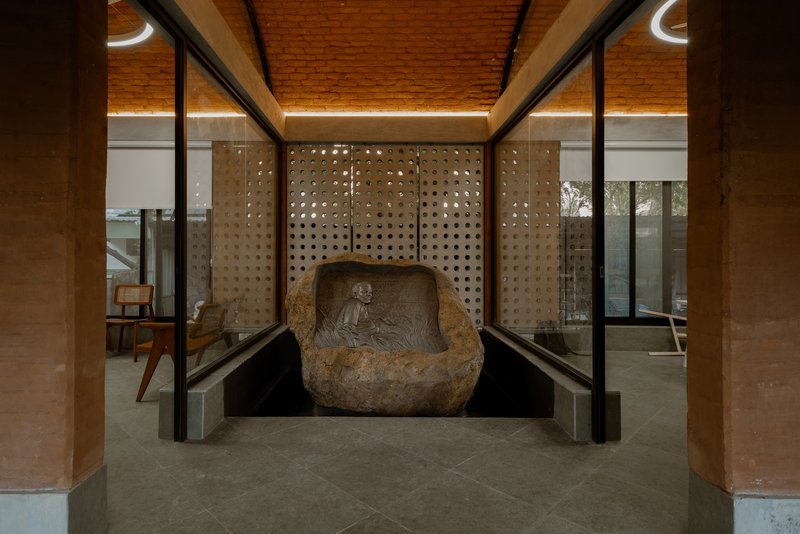 Carved stone sculpture set within a perforated wall niche flanked by glass partitions at dusk
