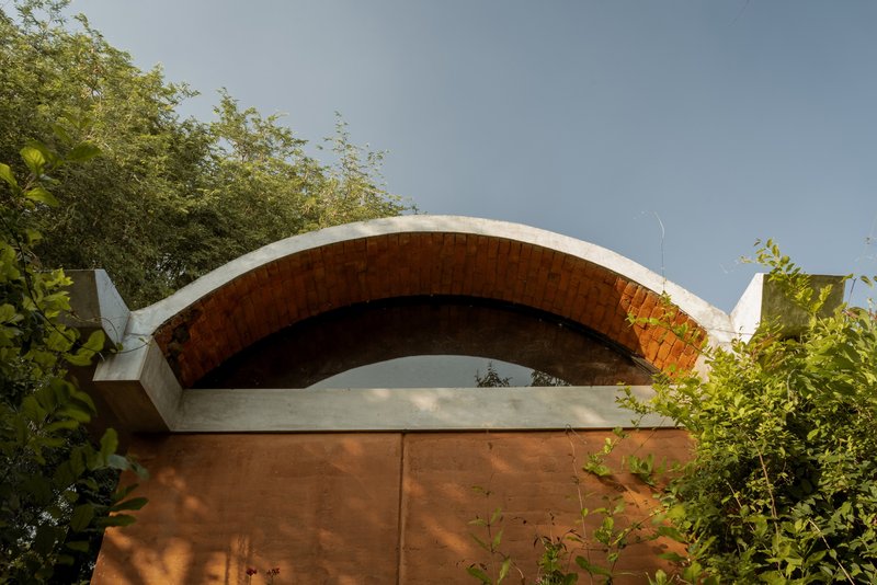 Exterior view of the exposed brick vault with concrete edge beam framed by foliage