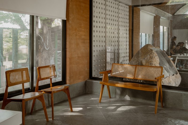 Seating nook with caned timber chairs and bench beside perforated stone screen wall in afternoon light