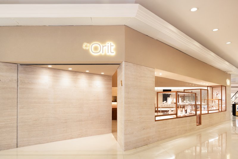 Storefront entrance clad in pale travertine with illuminated signage and polished white floor tiles