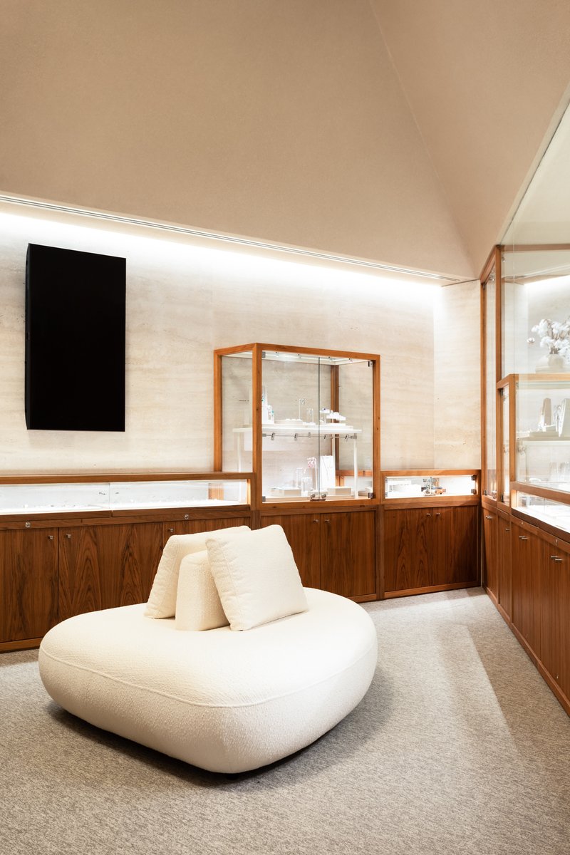 Curved seating beneath angled ceiling with walnut millwork and framed glass vitrines along the wall