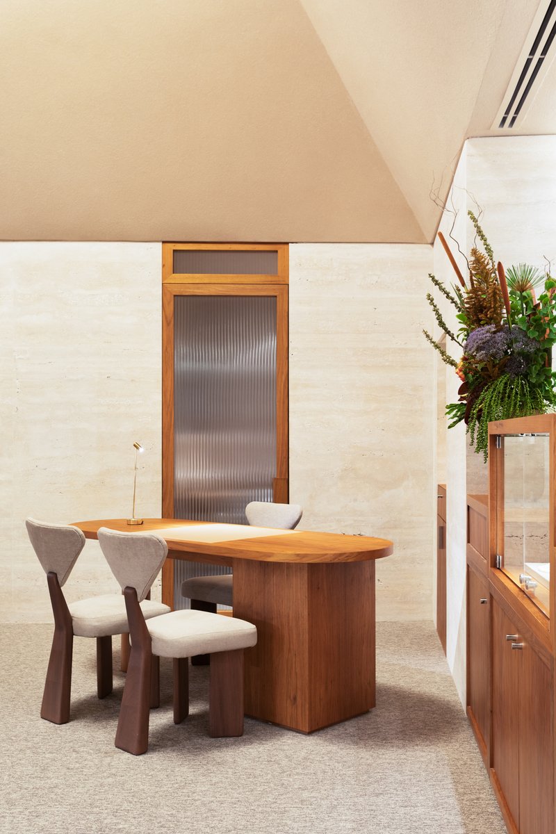 Walnut desk and upholstered chairs beneath a vaulted ceiling with concealed perimeter lighting