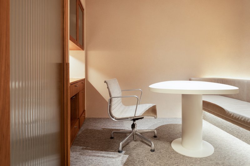 White pedestal table beside timber cabinetry with reeded glass panel under warm ambient light