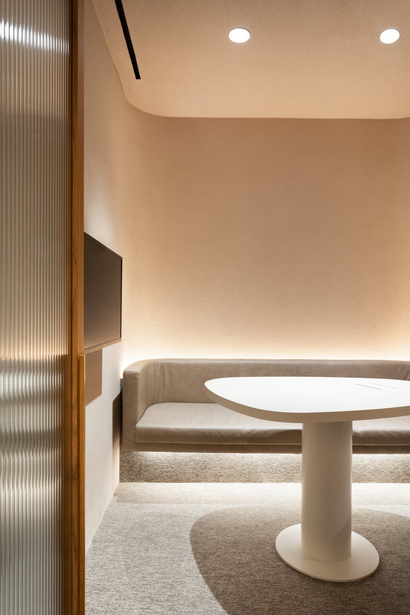Curved banquette seating around a white pedestal table with ribbed glass partition and recessed lighting