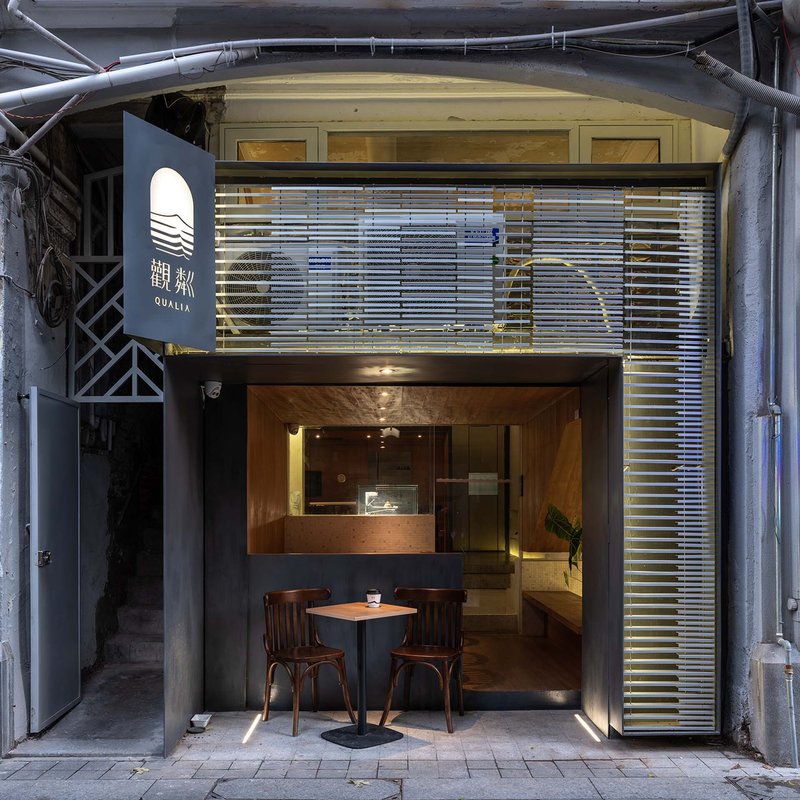 Street-level view of narrow storefront with horizontal metal louvers and warm interior lighting at dusk