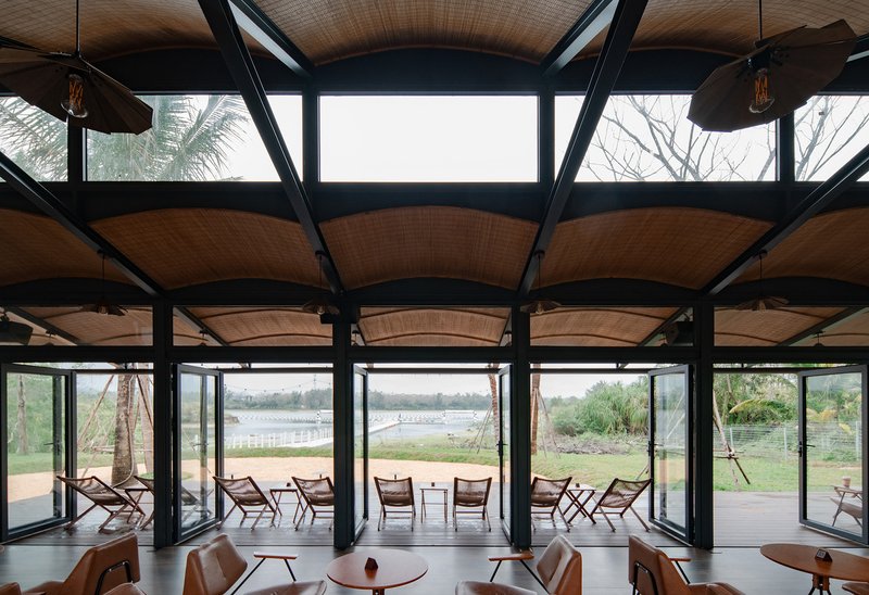 Interior view showing arched woven ceiling panels suspended between black steel trusses with clerestory windows above