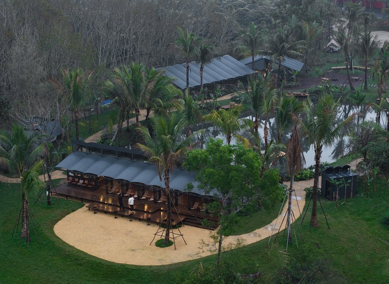 Aerial view of low pavilions with metal roofs amid palm trees and a central sand courtyard