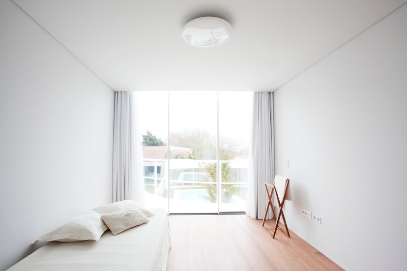 Bedroom with light wood flooring and glazed doors opening to a planted terrace beyond