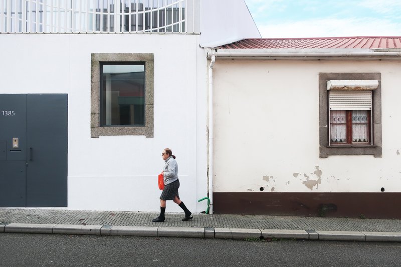Street view of white rendered facade with granite-framed window and grey door, person walking past