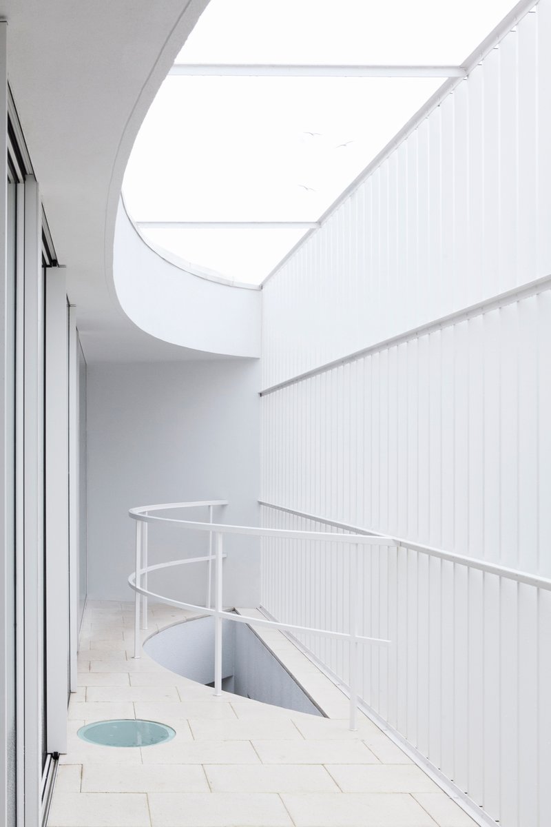 Upper terrace with curved roof overhang, tiled floor, metal balustrade, and skylight opening