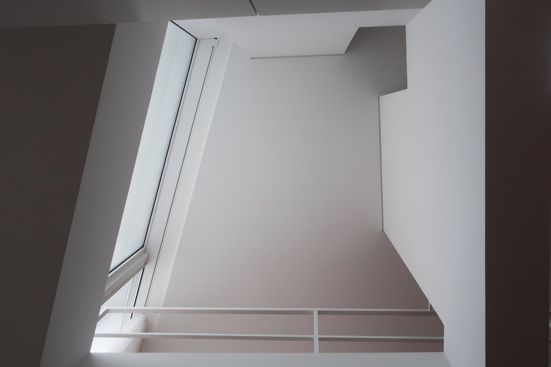 Upward view of a double-height void with angled clerestory windows and a white railing
