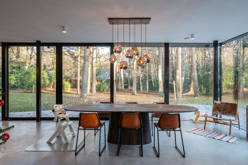 Dining area with full-height glazing overlooking woodland in late afternoon light
