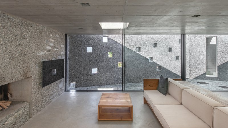 Living room with concrete ceiling and floor-to-ceiling glazing framing an interior courtyard with exposed concrete walls