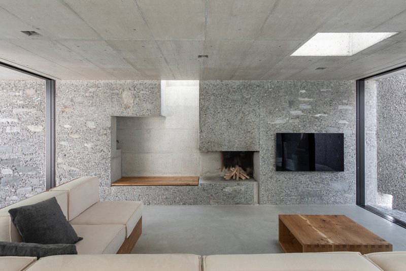 Fireplace and seating niche in aggregate concrete wall beneath skylight with exposed concrete ceiling